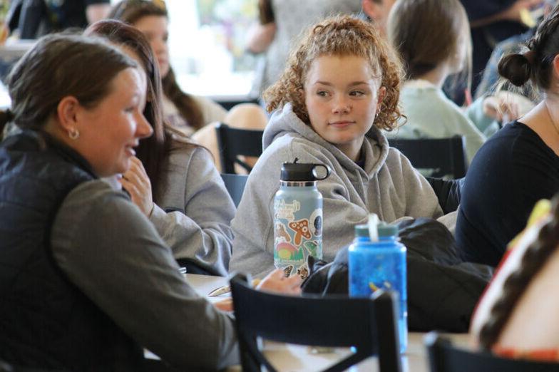 A female student listens to friends while sitting at a table in the Dining Hall